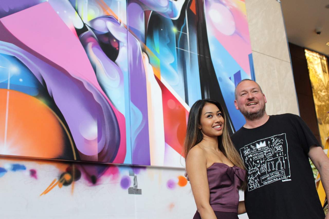 Artist Mr Cenz standing in front of his mural with muse, Maliha Islam